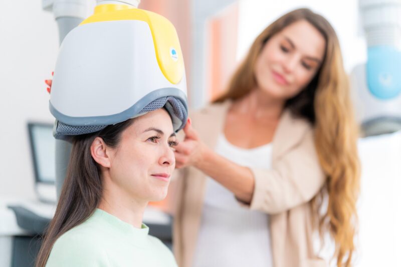 Clinician adjusting a BrainsWay helmet during a session with a patient, illustrating how TMS therapy for OCD is administered