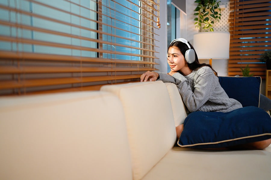 A relaxed woman wearing headphones looking out a window, representing positive signs TMS is working and improved mood.